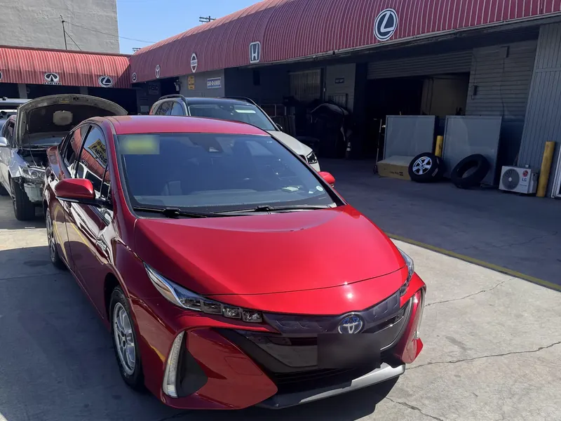 Red Prius after collision repair, parked in front of the shop bays