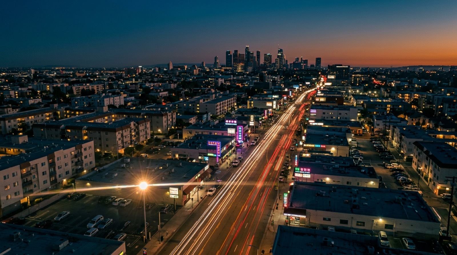 Aerial view of Koreatown Los Angeles at blue-hour dusk, Wilshire Boulevard light trails, downtown LA skyline in distance